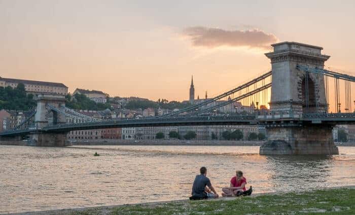 Two people relaxing in front of a bridge in Hungary, a country that offers easy citizenship by descent.