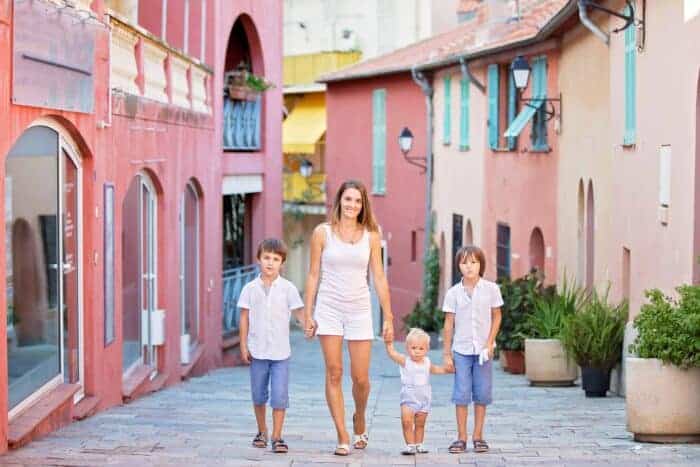 A young Expat mother with her three children walking down a colorful street in Europe.
