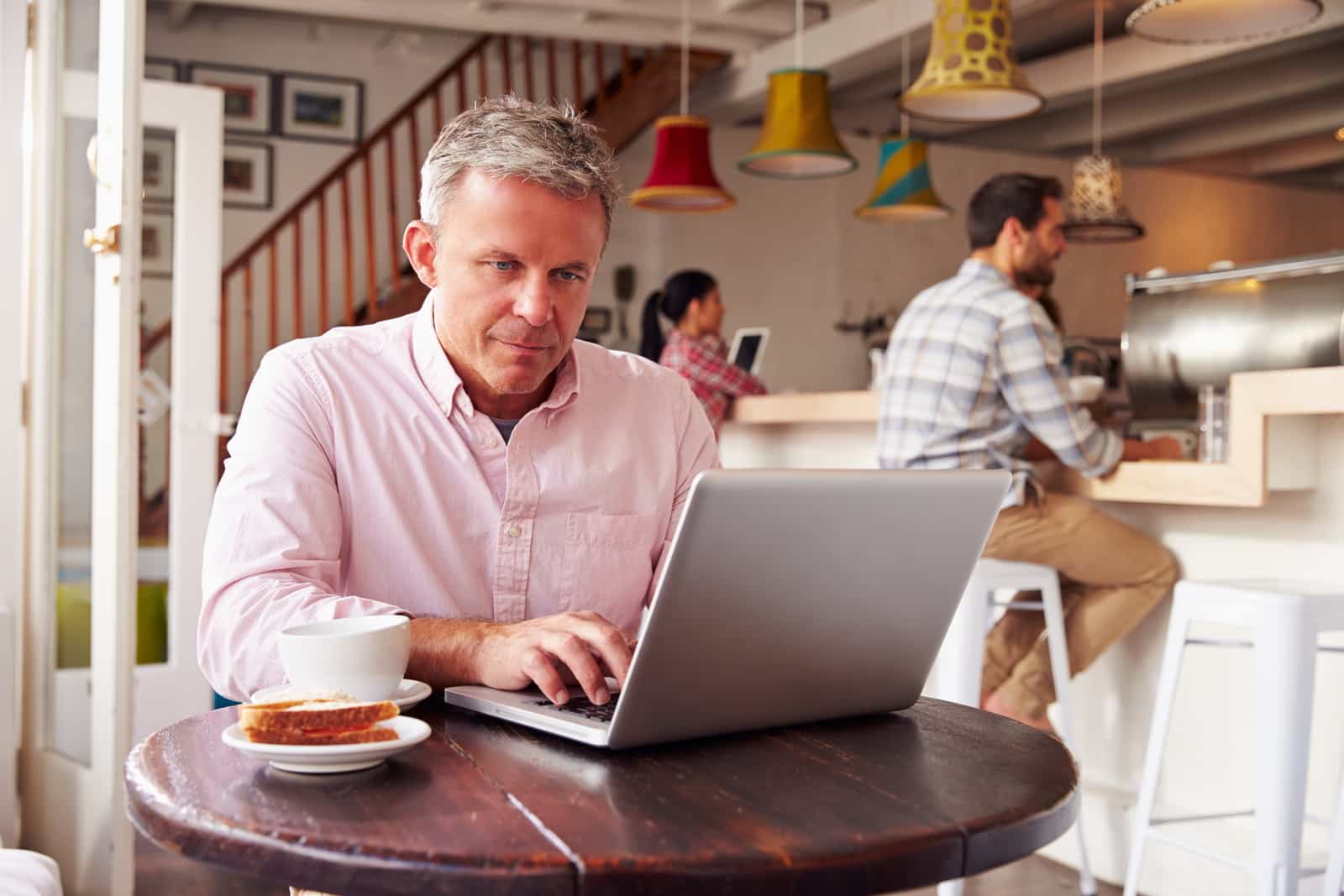 a middle aged man in a cafe making an international money transfer on his laptop